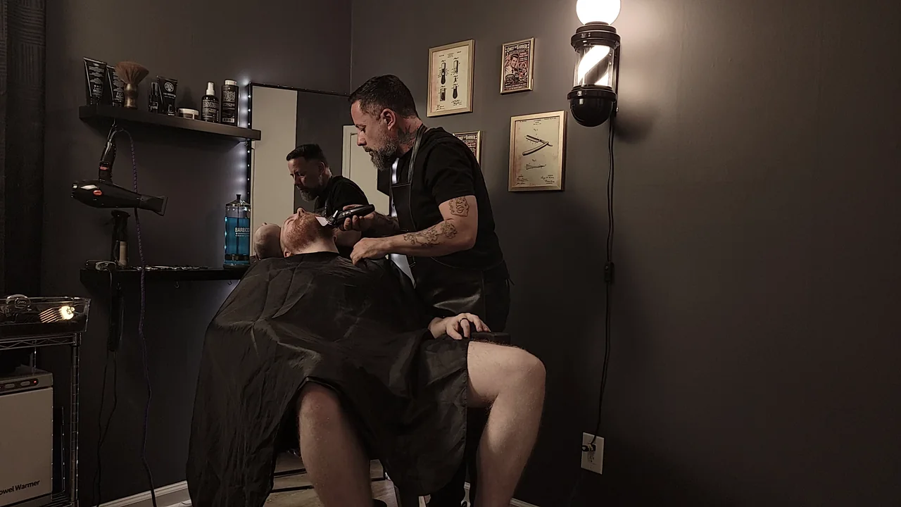 The Barber in a black apron detailing a client's beard in the studio