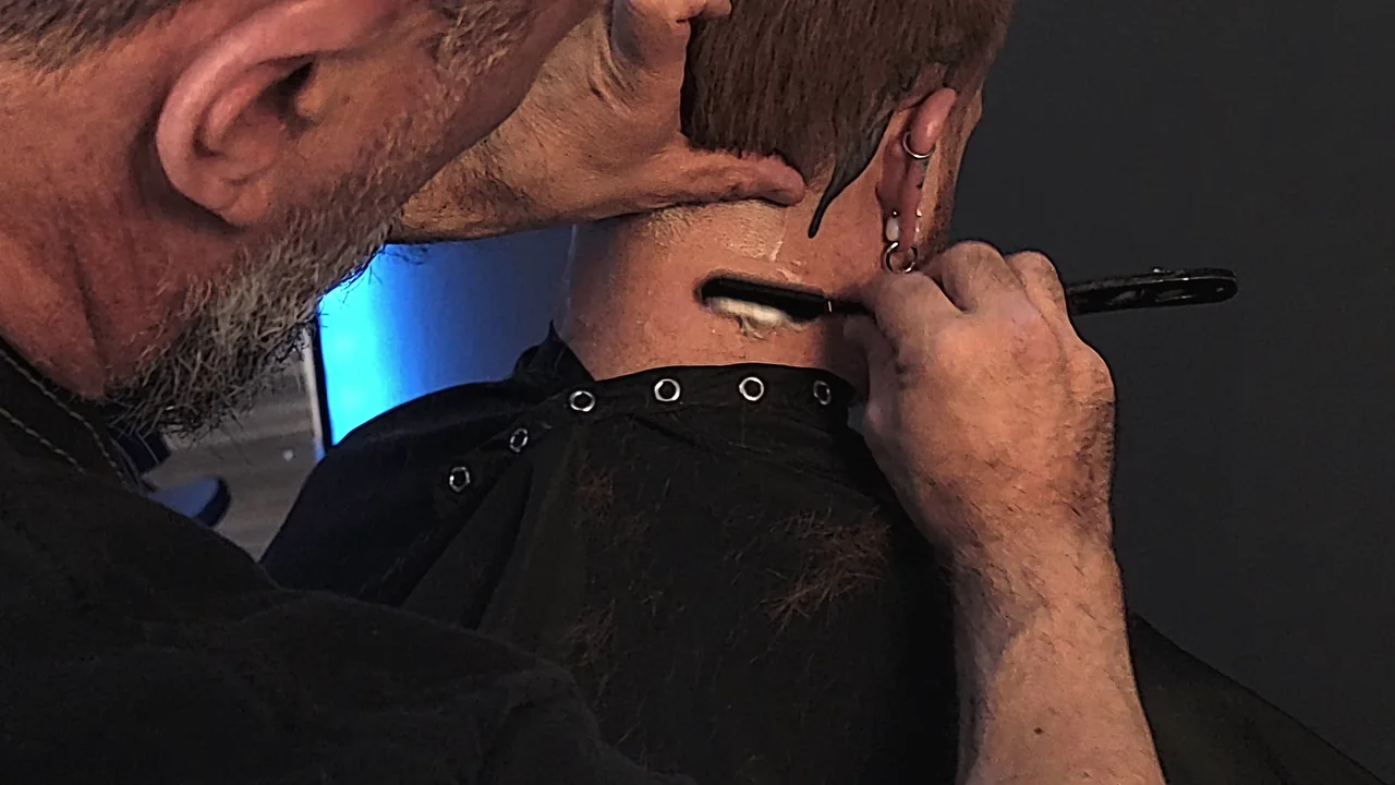 A close-up of a straight razor carefully finishing the back of a haircut