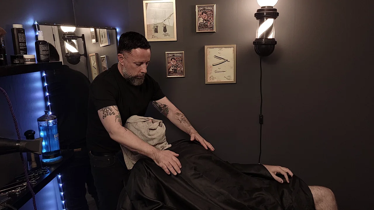 The Barber preparing a warm towel treatment for a caped client